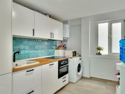 Moderne Küche mit weißen Schränken, heller Holztheke und einem lebhaften türkisfarbenen Fliesenspiegel. Mit integrierten Geräten und einem Hauswirtschaftsbereich mit Waschmaschine.