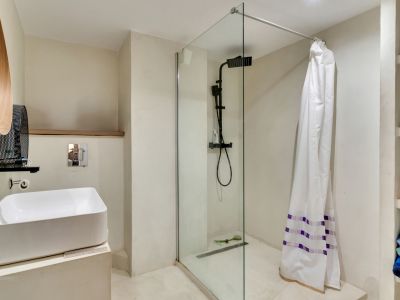 Modernes Badezimmer mit Aufsatzwaschbecken, mattschwarzen Armaturen und ebenerdiger Dusche mit Glaswand. Einzigartiger Holzspiegel und integrierte Regale.