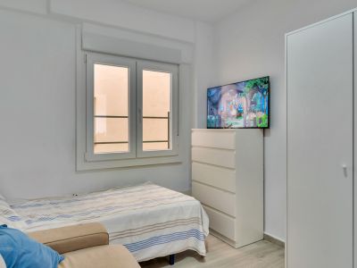 Nebenzimmer mit Einzelbett, weißem Einbauschrank und Kommode mit Wandfernseher. Das Doppelfenster sorgt für natürliches Licht.