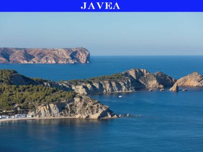 Panoramablick auf Jáveas zerklüftete Küste, mit pinienbewachsenen Klippen, einer abgelegenen Bucht mit weißen Häusern und felsigen Inseln im blauen Mittelmeer, sowie einem entfernten Leuchtturm.