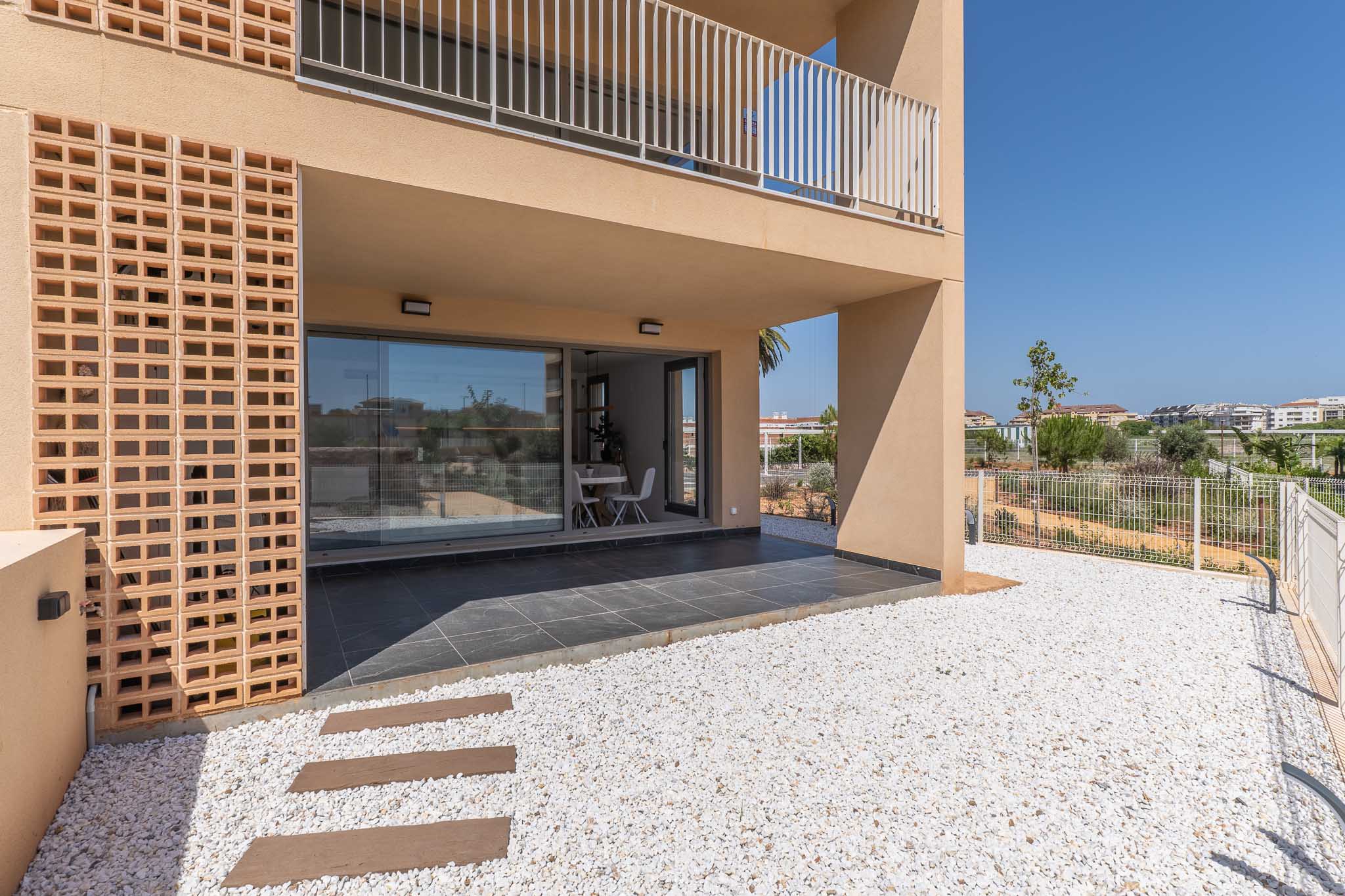 Überdachte Erdgeschoss-Terrasse mit dunklen Fliesen, direkt verbunden mit einem privaten Garten aus weißem Kies. Große Glastüren zeigen einen hellen Essbereich im Inneren, ergänzt durch eine moderne Ziegelfassade.