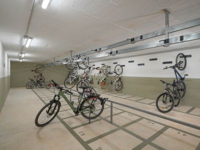 Geräumiger Gemeinschafts-Fahrradabstellbereich mit nummerierten Bodenplätzen und Wandhalterungen. Hell beleuchtet durch Deckenleuchten, bietet er sichere Aufbewahrung im Wohnkomplex.