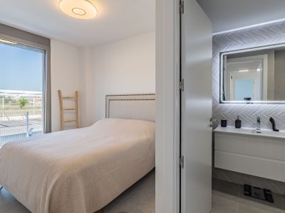 Geräumiges Schlafzimmer mit gepolstertem Kopfteilbett und direktem Zugang zur Außenterrasse. Ein en-suite Badezimmer mit schwebendem Waschtisch und beleuchtetem Spiegel ist sichtbar.