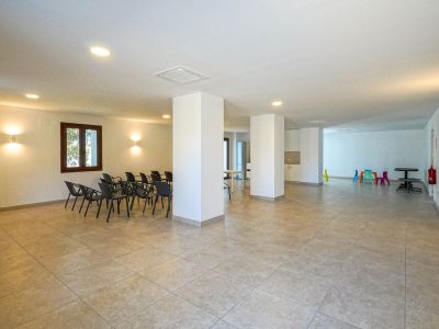 Großer Gemeinschaftsraum mit Fliesenboden, tragenden Säulen und Einbauleuchten. Bietet einen Bestuhlungsbereich für Treffen und eine bunte Kinderspielecke.