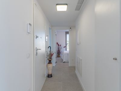 Heller, moderner Flur mit hellgrauen Fliesen und weißen Wänden. Ausgestattet mit Sicherheitspanel, moderner Deckenleuchte und Blick in ein Schlafzimmer.