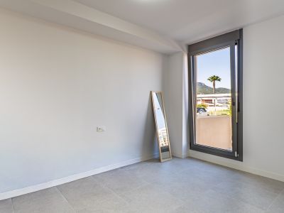 Leerer Raum mit weißen Wänden und grauen Fliesen, bereit zur individuellen Gestaltung. Großes Fenster mit Blick auf eine Palme und Berge, das viel Tageslicht spendet.