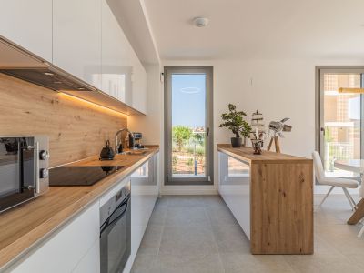 Moderne offene Küche mit glänzenden weißen Schränken, Arbeitsplatten und Spritzschutz in Holzoptik. Integrierte Geräte, LED-Beleuchtung und direkter Zugang zum Außenbereich.