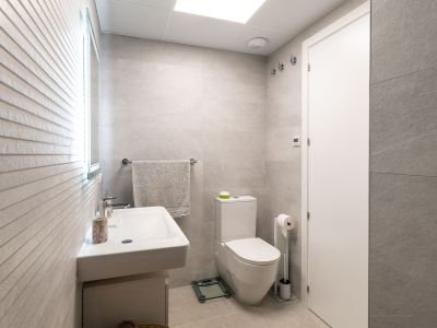 Modernes Badezimmer mit hellgrauen Großformatfliesen, Hänge-Waschbecken und WC. Ein beleuchteter Spiegel akzentuiert die strukturierte Wand.