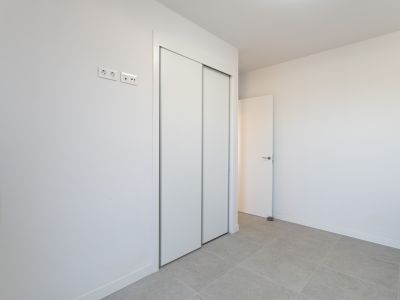 Schlafzimmer mit großem Einbauschrank mit weißen Schiebetüren und hellem Fliesenboden. Moderne Strom- und Datenanschlüsse sind vorhanden.