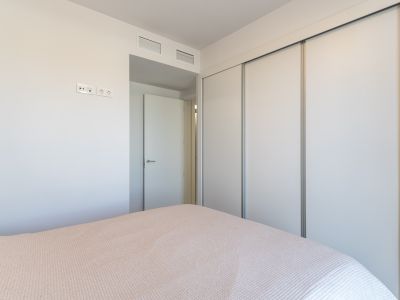 Schlafzimmeransicht mit einem geräumigen Einbauschrank mit weißen Schiebetüren. Die Wand zeigt moderne Steckdosen und integrierte Lüftungsgitter über der angrenzenden Tür.