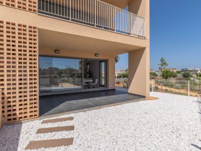 Überdachte Erdgeschoss-Terrasse mit dunklen Fliesen, direkt verbunden mit einem privaten Garten aus weißem Kies. Große Glastüren zeigen einen hellen Essbereich im Inneren, ergänzt durch eine moderne Ziegelfassade.