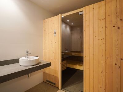 Umkleidebereich mit einem eleganten, schwebenden Waschtisch und Aufsatzwaschbecken sowie dem Holztür-Eingang zur Sauna mit Glaspaneel.