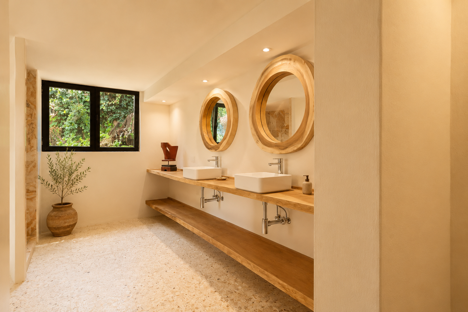 Badezimmer mit doppeltem Holzwaschtisch, zwei weißen rechteckigen Waschbecken und großen runden Spiegeln mit Naturholzrahmen. Ein Fenster blickt auf üppiges Grün, passend zum hellen Terrazzoboden.