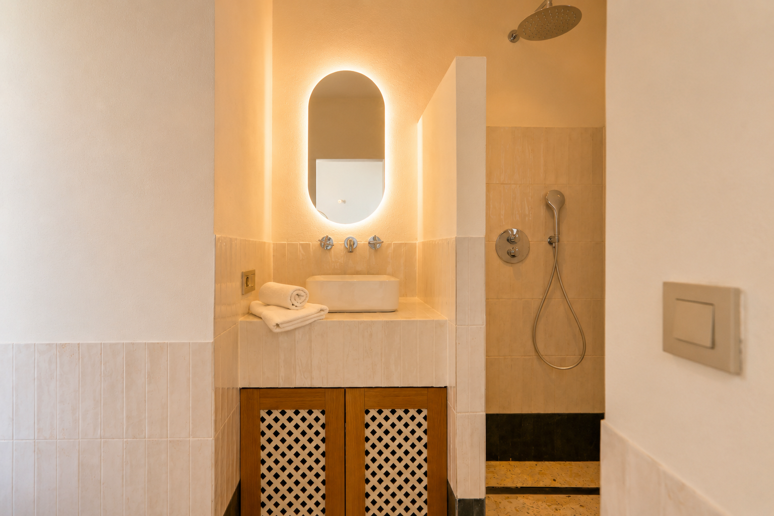 Dieses elegante Badezimmer bietet einen Aufsatzwaschtisch, einen ovalen, hinterleuchteten Spiegel und einen Holzschrank mit Gittertüren. Die Dusche hat einen Regenduschkopf.