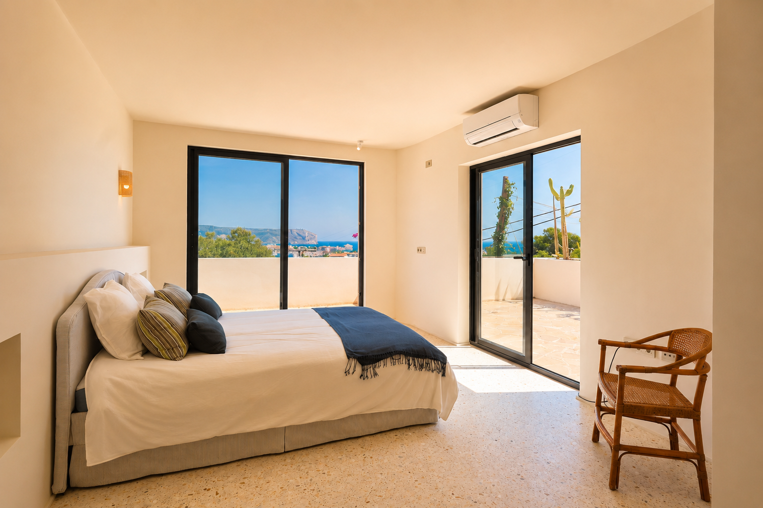 Helles Schlafzimmer mit hellem Terrazzoboden und großen Glasschiebetüren, die zu einer privaten Terrasse führen. Es bietet weite Ausblicke auf das Meer und die ferne Küste.