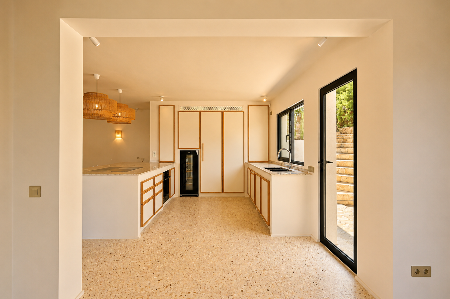 Moderne Küche mit hellen Holzrahmenfronten, Terrazzo-Boden und einer großen Kochinsel. Geflochtene Pendelleuchten beleuchten den Raum.