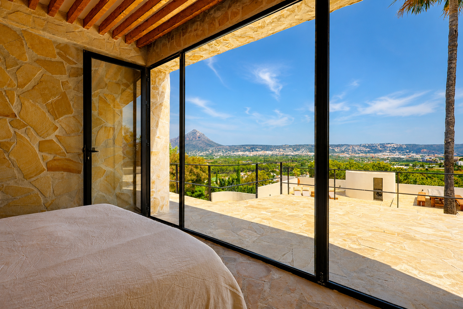 Schlafzimmer mit Natursteinwänden und Holzbalken, direktem Zugang zur Terrasse mit Panoramablick auf den Montgó und die Bucht von Jávea.