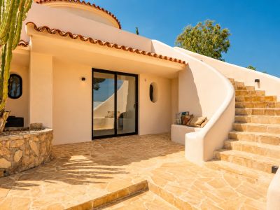 Außenpatio mit warm getöntem, unregelmäßigem Steinpflaster, einer geschwungenen Treppe und einem großen Kaktus. Mit Glasschiebetür und integrierter Sitzbank in der Stuckwand.