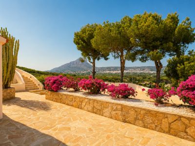 Außenterrasse mit Natursteinpflaster, geschwungener Treppe und leuchtenden Bougainvilleen. Ein großer Kaktus und Panoramablick auf Berge und die Stadt.