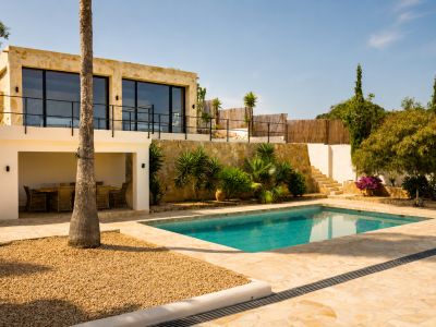 Die terrassierte Villa außen zeigt einen rechteckigen Pool mit unregelmäßigem Steinpflaster, einen überdachten Essbereich und eine Steinfassade mit großen Fenstern.