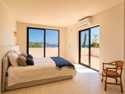 Helles Schlafzimmer mit hellem Terrazzoboden und großen Glasschiebetüren, die zu einer privaten Terrasse führen. Es bietet weite Ausblicke auf das Meer und die ferne Küste.