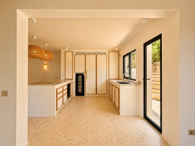 Moderne Küche mit hellen Holzrahmenfronten, Terrazzo-Boden und einer großen Kochinsel. Geflochtene Pendelleuchten beleuchten den Raum.