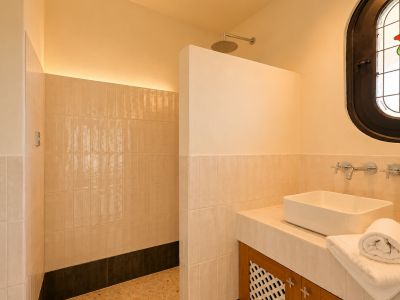 Modernes Badezimmer mit ebenerdiger Dusche, Regenduschkopf und indirekter LED-Beleuchtung. Aufsatzwaschbecken auf gefliester Ablage und ovales Buntglasfenster mit Rosenmotiv.