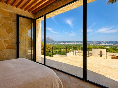 Schlafzimmer mit Natursteinwänden und Holzbalken, direktem Zugang zur Terrasse mit Panoramablick auf den Montgó und die Bucht von Jávea.