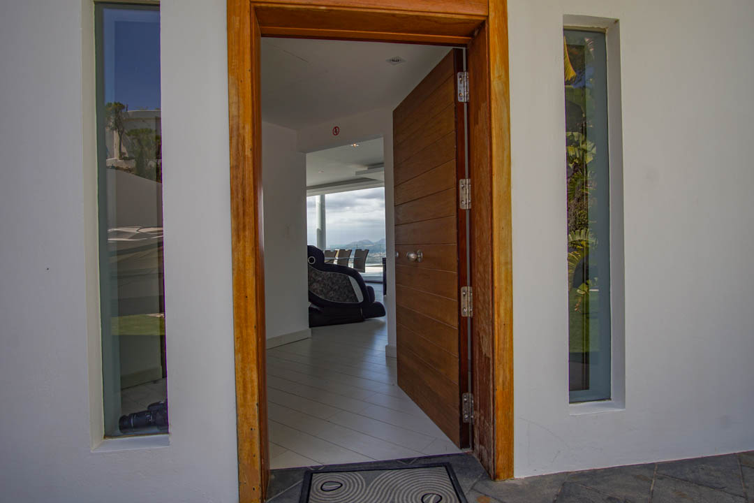 Der offene Haupteingang zeigt eine getäfelte Holztür mit Rahmen, flankiert von vertikalen Fenstern, und bietet einen Einblick in das moderne Interieur mit Bergblick.