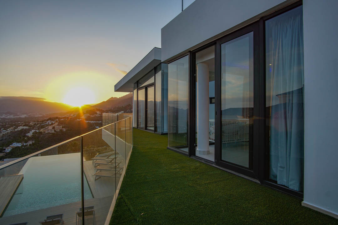 Die großzügige Terrasse mit Infinity-Pool, Holzdeck und Glasbrüstung bietet einen Panoramablick auf den Sonnenuntergang über Berge und Tal.