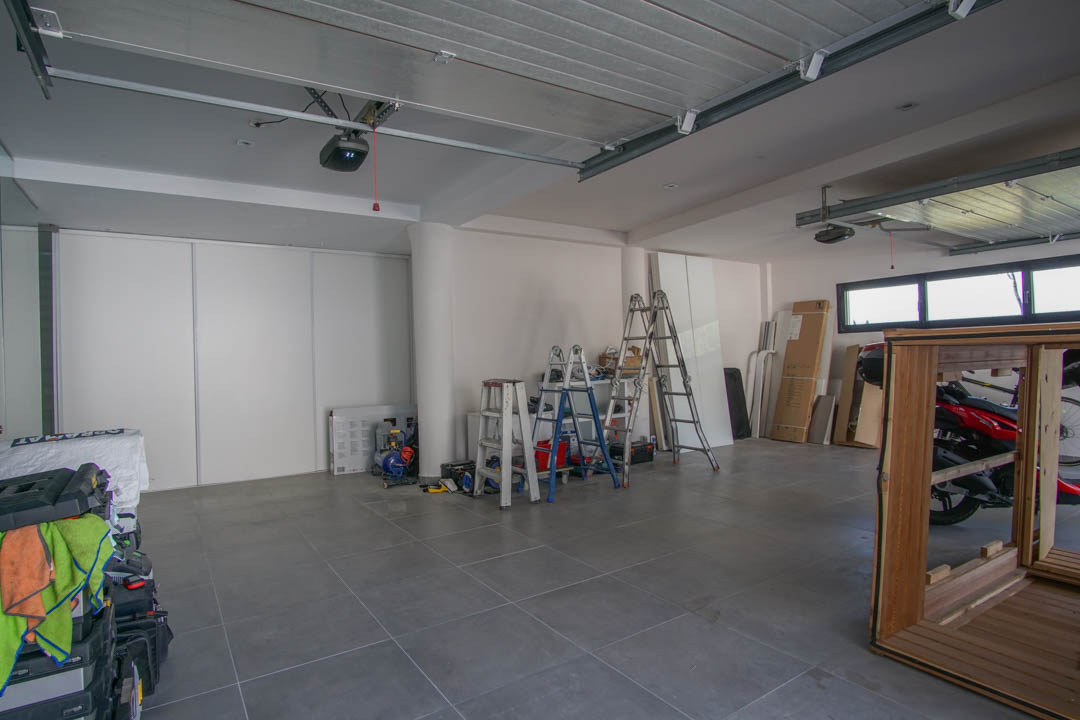 Geräumige Garage mit grauem Fliesenboden und weißen Wänden. Ausgestattet mit zwei automatischen Torantrieben, horizontalen Fenstern und weißen Schiebetüren für Stauraum.
