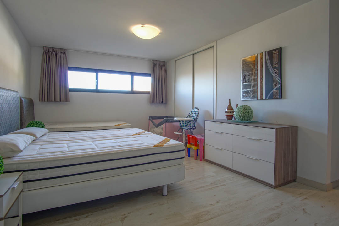 Helles Schlafzimmer mit einem Bett aus zwei Matratzen, hellem Holzfußboden und einem langen Querfenster. Es verfügt über einen weißen Schiebetürenschrank und eine moderne Kommode mit abstrakter Kunst.