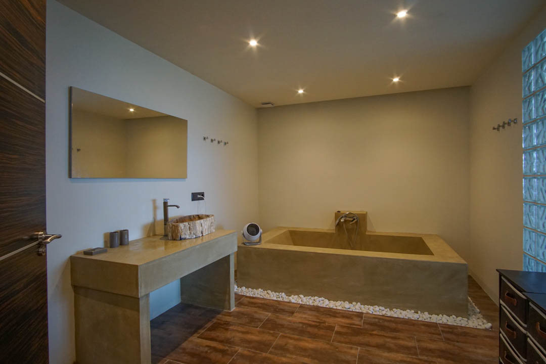Modernes Badezimmer mit rustikalem Holzwaschbecken auf Betonoptik-Waschtisch, integrierter Wanne und Glasbausteinwand.