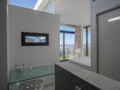 Arbeitsbereich mit Glasschreibtisch und horizontalem Fenster, der vom angrenzenden Schlafzimmer aus einen Panoramablick auf Meer und Stadt bietet.
