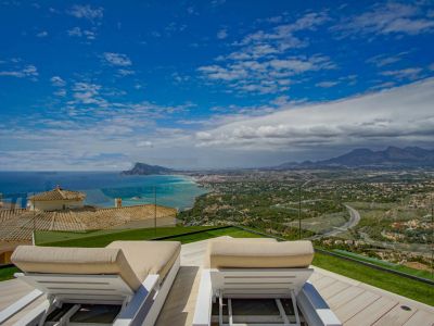 Dachterrasse mit zwei weißen Sonnenliegen auf hellem Holzdeck und Kunstrasen, mit Panoramablick auf das Mittelmeer, die Küste von Altea und ferne Berge.
