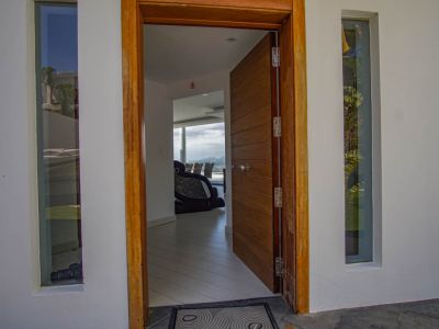 Der offene Haupteingang zeigt eine getäfelte Holztür mit Rahmen, flankiert von vertikalen Fenstern, und bietet einen Einblick in das moderne Interieur mit Bergblick.