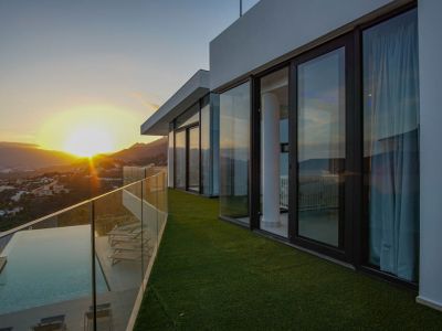 Die großzügige Terrasse mit Infinity-Pool, Holzdeck und Glasbrüstung bietet einen Panoramablick auf den Sonnenuntergang über Berge und Tal.