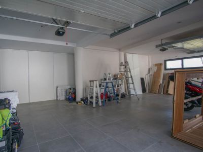 Geräumige Garage mit grauem Fliesenboden und weißen Wänden. Ausgestattet mit zwei automatischen Torantrieben, horizontalen Fenstern und weißen Schiebetüren für Stauraum.