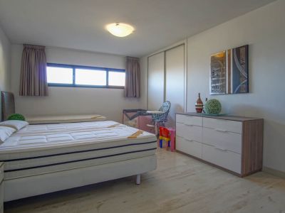 Helles Schlafzimmer mit einem Bett aus zwei Matratzen, hellem Holzfußboden und einem langen Querfenster. Es verfügt über einen weißen Schiebetürenschrank und eine moderne Kommode mit abstrakter Kunst.