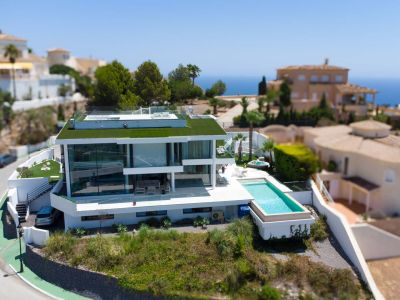 Luftaufnahme der modernen weißen Designervilla mit Gründach, Infinity-Pool und separatem Whirlpool, eingebettet in eine Umgebung mit Meerblick.