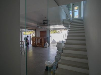Moderne Innentreppe mit Glasgeländer und hellen Stufen, angrenzend an eine geflieste Garage mit offenem Tor und natürlichem Lichteinfall.