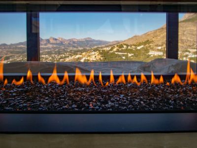 Moderner Gaskamin mit Flammen über dunklem Glasgranulat, der einen Panoramablick auf Berge und Tal freigibt.