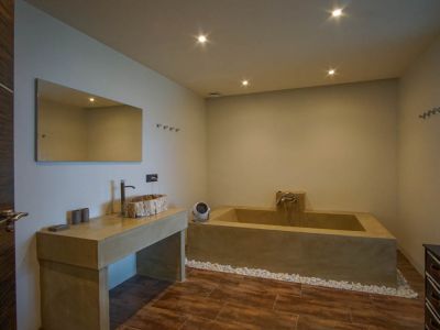 Modernes Badezimmer mit rustikalem Holzwaschbecken auf Betonoptik-Waschtisch, integrierter Wanne und Glasbausteinwand.