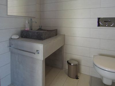 Modernes Gäste-WC mit Steinwaschbecken auf Betonoptik-Waschtisch und hellen Fliesen. Wandhängendes WC mit Chrom-Spülplatte.