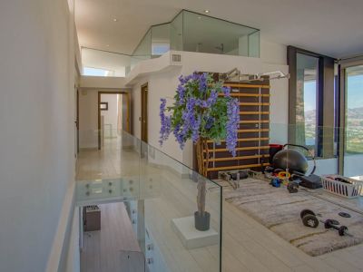 Obergeschoss-Fitnessbereich mit modernen Glasgeländern und hellem Boden. Ausgestattet mit Sprossenwand und Gewichten, bietet er Panoramablicke durch raumhohe Fenster.