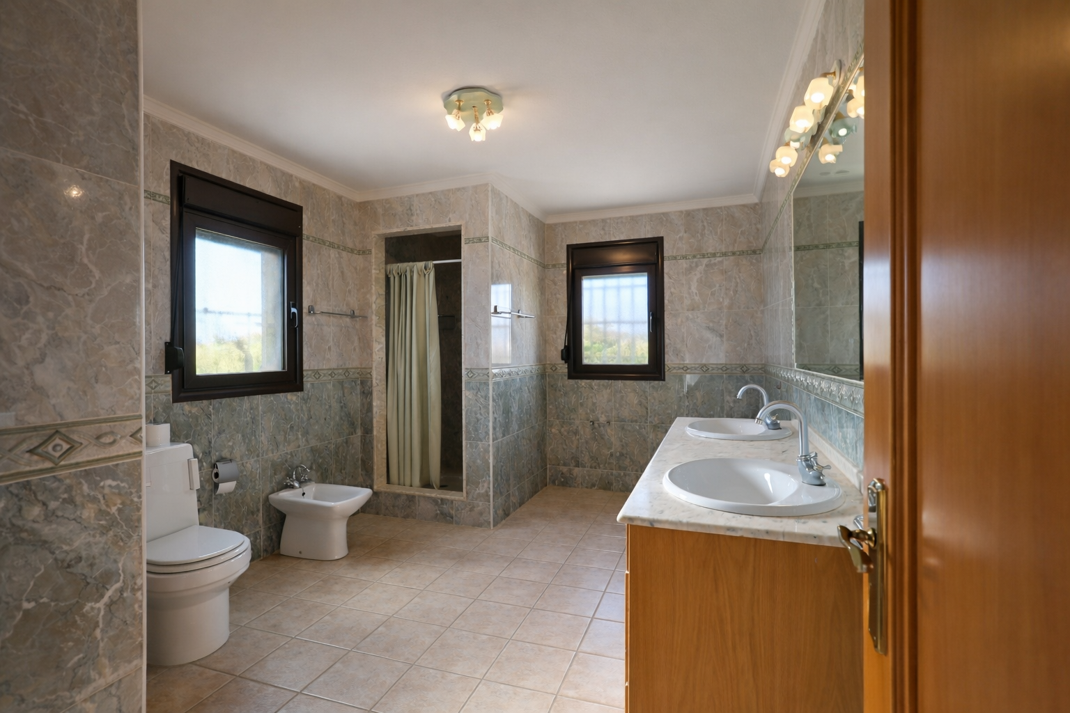 Geräumiges Badezimmer mit Doppelwaschtisch auf Marmorplatte und Holzunterschrank. Ausgestattet mit ebenerdiger Dusche, WC, Bidet und zwei Fenstern für Tageslicht.
