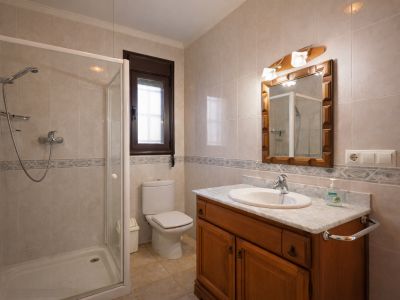 Badezimmer mit Duschkabine, WC und einem Holzwaschtisch mit Marmorplatte. Die Wände sind mit hellen Fliesen und einer dekorativen Bordüre versehen.
