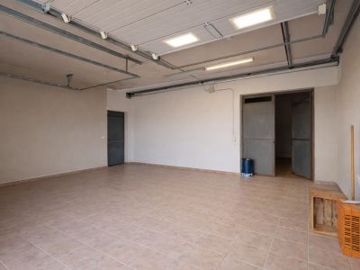 Geräumige Garage oder Hauswirtschaftsraum mit hellen Fliesen, industrieller Deckenbeleuchtung und mehreren Zugängen.