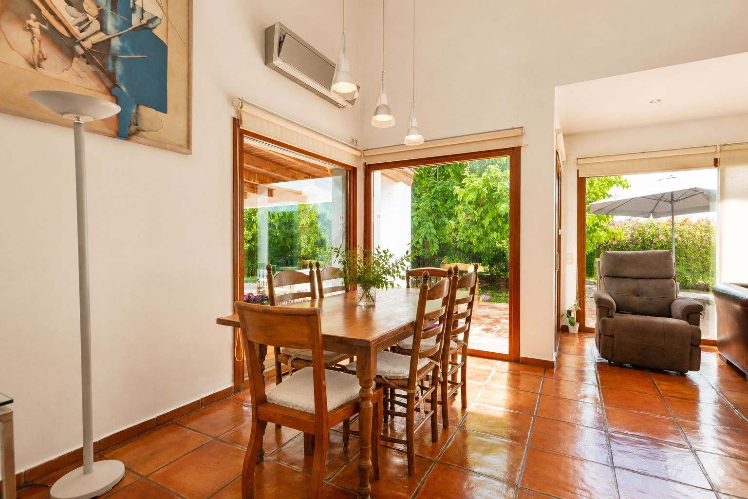 Helles Hauptwohnzimmer mit handgefertigten Terrakottaböden, einem markanten doppelseitigen Kamin und großen Fenstern, die den Raum mit natürlichem Licht und mediterranem Flair erfüllen.