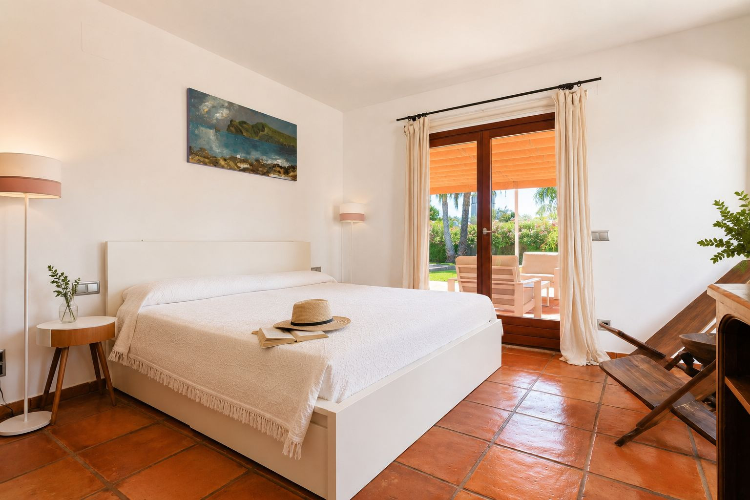 Helles Schlafzimmer mit weißem Bett, handgefertigten Terrakottaböden und direktem Zugang zur Außenterrasse mit Gartenblick.